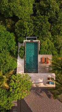 Aerial view of a turquoise swimming pool surrounded by lush tropical trees, a wooden deck with lounge chairs, and a stone patio in San Miguel, Provincia de Guanacaste, Costa Rica.