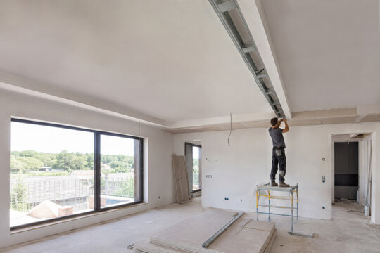 Trabajo en interiores de una habitaci&oacute;n moderna con ventanas grandes y un trabajador en una escalera