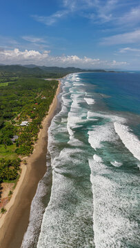 Aerial view of the coastline at San Miguel with lush tropical vegetation, palm trees, and rolling waves crashing onto the beach in San Miguel, Provincia de Guanacaste, Costa Rica.