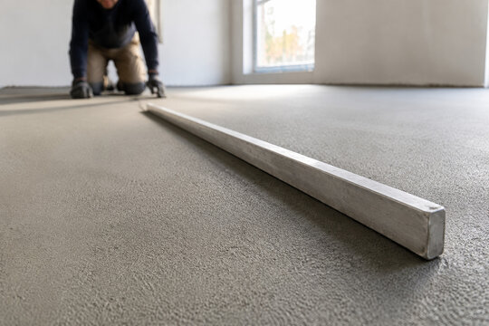 Trabajador en la construcci&oacute;n nivelando el suelo en una habitaci&oacute;n con luz natural