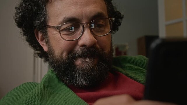 Middle aged Caucasian man with glasses smiling while scrolling on smartphone. Clip is perfect for mobile app marketing, digital communication ads, and modern lifestyle commercial videos