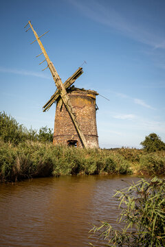 Derelict brick windmill beside a Norfolk waterway under clear blue sky
