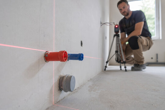 Un trabajador mide y marca las instalaciones en una pared usando un l&aacute;ser en una obra de construcci&oacute;n