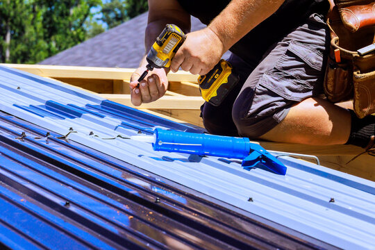 Worker installs metal roof using drill sealant in residential area
