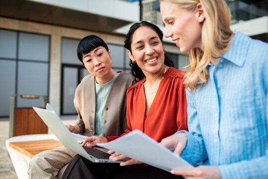 Three businesswomen collaborating with laptop outdoors