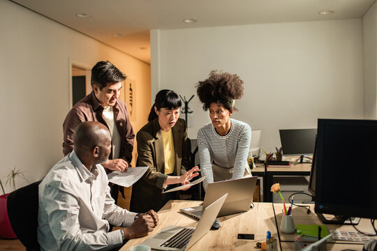 Diverse coworkers collaborating at laptops in modern office