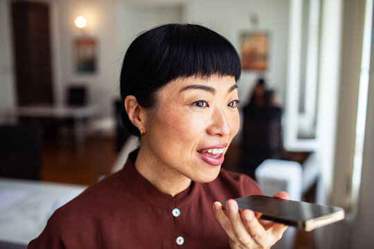 Smiling woman using voice assistant at home office