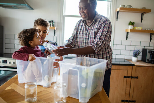 Grandfather helping children recycle plastic bottles in home kitchen