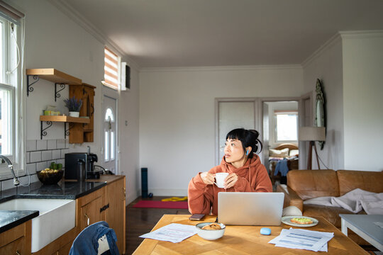 Woman working from home at kitchen table with laptop and coffee