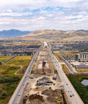 Aerial view of the 2100 North Freeway construction site, featuring heavy machinery, earthworks, and suburban development with mountains in the background in Lehi, Utah, United States.
