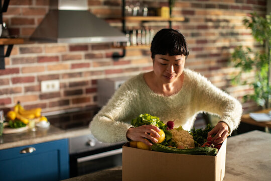 Woman unpacking fresh produce delivery box in home kitchen