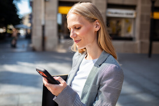Smiling businesswoman checking smartphone on urban street