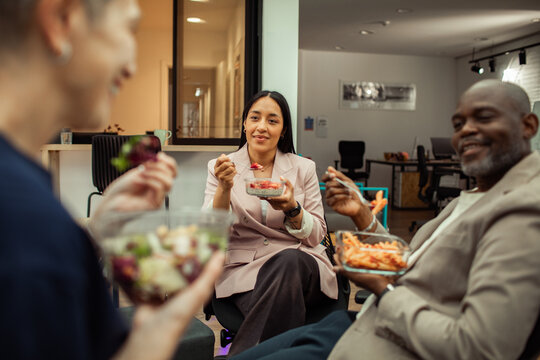 Diverse coworkers eating lunch together in modern office break room