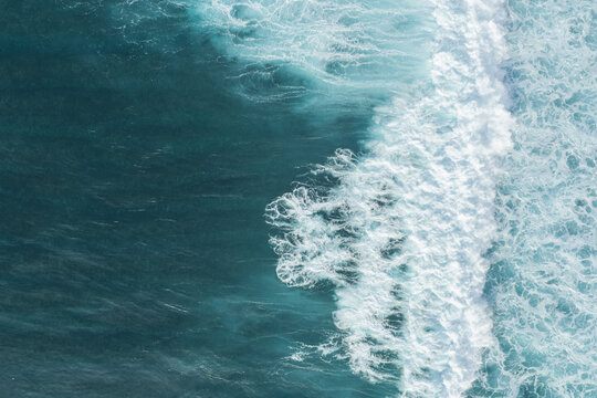 Aerial view of turquoise ocean waves with white sea foam patterns in Bali, Indonesia.