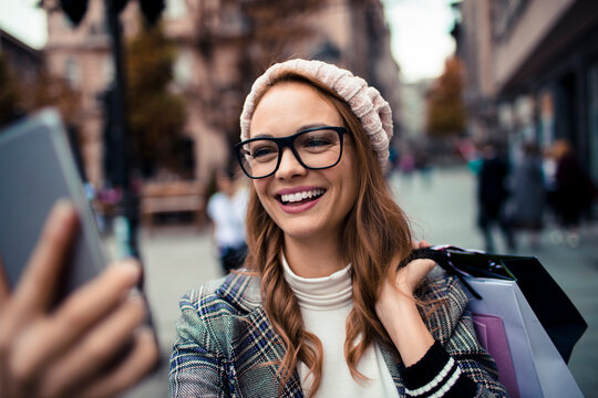 Smiling young woman taking a selfie while shopping on a city street