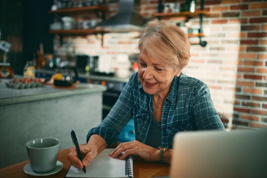 Smiling senior woman writing notes at kitchen table