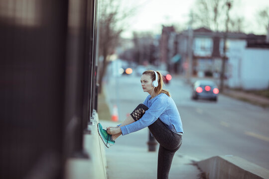 Young woman stretching before run on city sidewalk