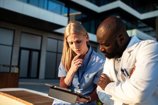 Doctor and nurse reviewing patient data on tablet outside hospital