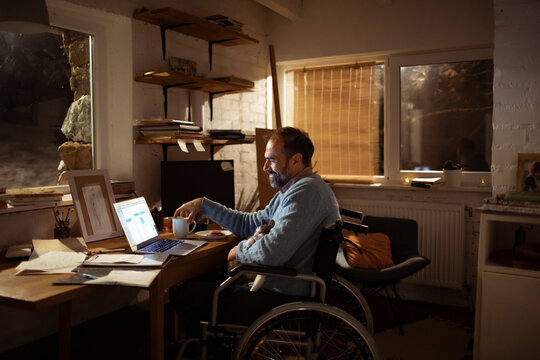 Man in wheelchair working on laptop at home office at night