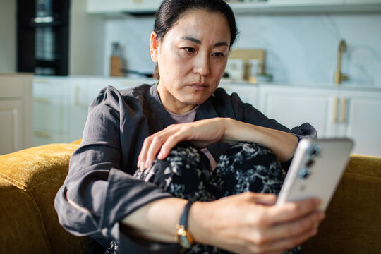 Concerned woman reading smartphone on sofa at home