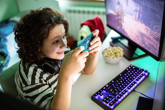 Kid gaming on smartphone at home computer desk
