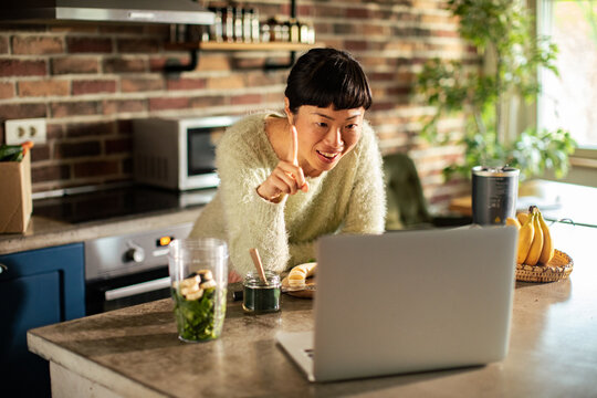 Woman making smoothie during video call in home kitchen
