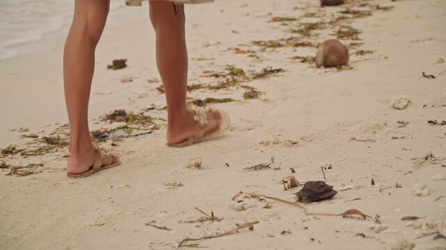 Bare feet walking along sandy beach, toes sinking into warm grains, stepping around coconut and coral fragments, gentle tide brushing ankles, hem of embroidered dress fluttering, quiet grounding