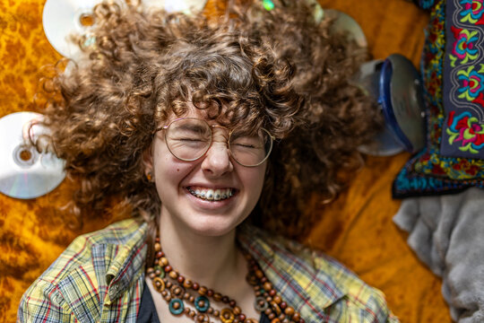 A smiling teenage girl with curly hair enjoys music indoors