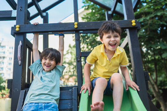 Smiling boys play on a playground slide outdoors in summer