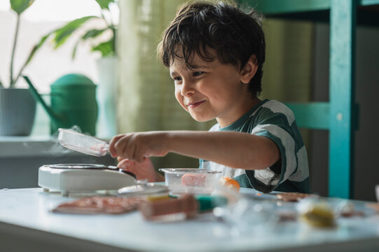 Smiling boy cooking with toy kitchen and steam indoors