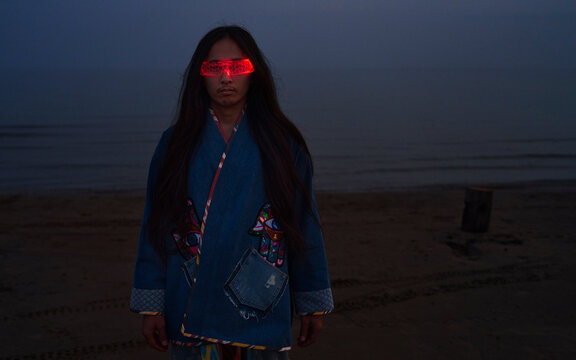 Man in traditional robe wears VR glasses on the beach at sunset
