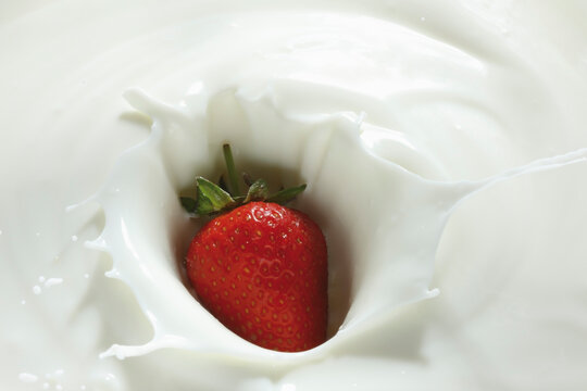 Strawberry dropping into yogurt, close up