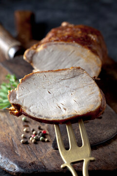 A slice of rolled roast pork rests on a fork above a wooden board