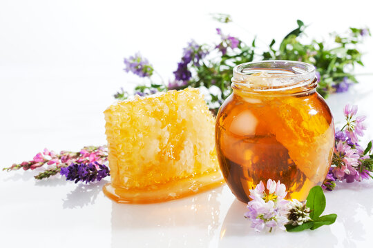 Glass of blossom honey with honeycomb and blossoms on white ground