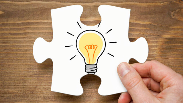 Hand holding a white puzzle piece with a hand-drawn glowing lightbulb icon representing creative problem solving and innovative business ideas
