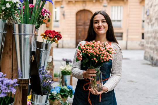 Young female florist holding Hypericum flower vase while standing at flower shop
