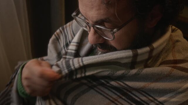 Middle-aged Caucasian man putting on eyeglasses and wrapping plaid blanket around shoulders while looking down. Clip is ideal for promoting vision care, healthy aging, or home wellness products