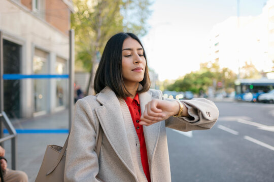 A businesswoman checks her watch while waiting for the bus outdoors
