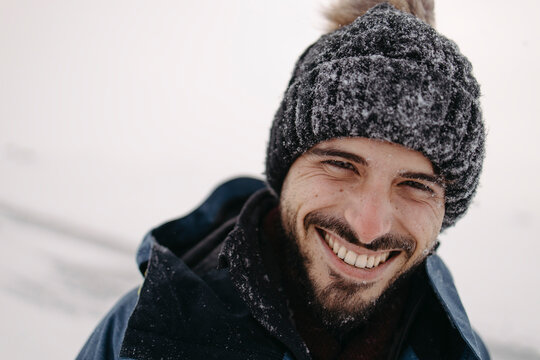 Smiling man with beard wears winter hat in snowy Lapland landscape