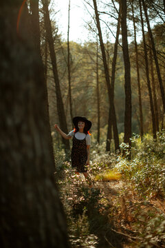 A smiling woman wears a black hat in a sunny forest