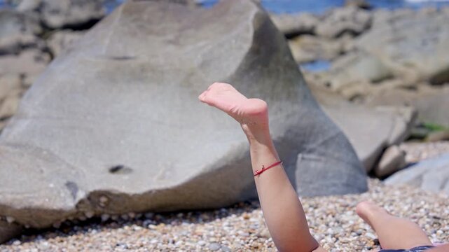 Woman wiggling her foot while sunbathing on a pebble beach