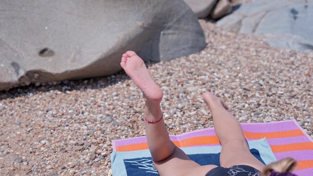 Woman playfully moving her legs while sunbathing on a pebble beach towel
