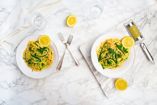 Two plates feature lemon zucchini pasta on a marble table