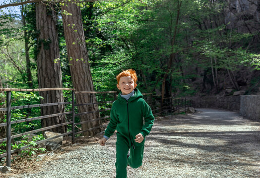 A smiling red-haired boy runs through the green forest