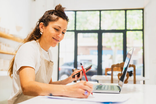 Smiling entrepreneur manages billing at laptop in pottery workshop