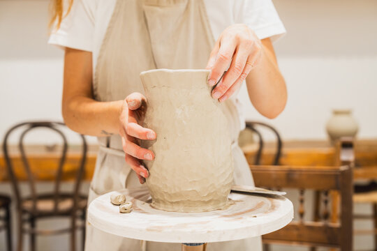 Woman shaping a clay vase on a pottery wheel in a workshop