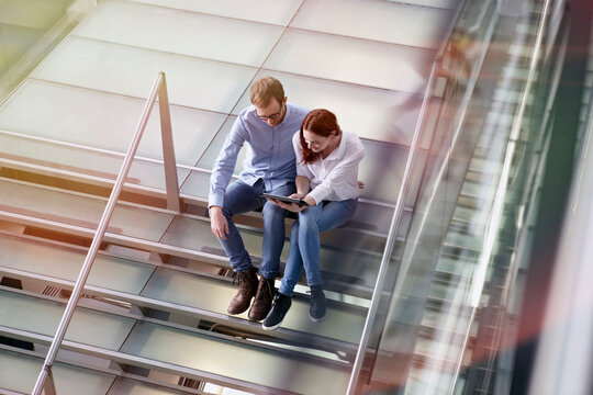 Germany, Cologne, Young woman and mid adult man with tablet at stairs