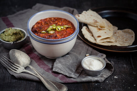 Tortillas and bowls of guacamole, sour cream, Chili con carne on wooden table