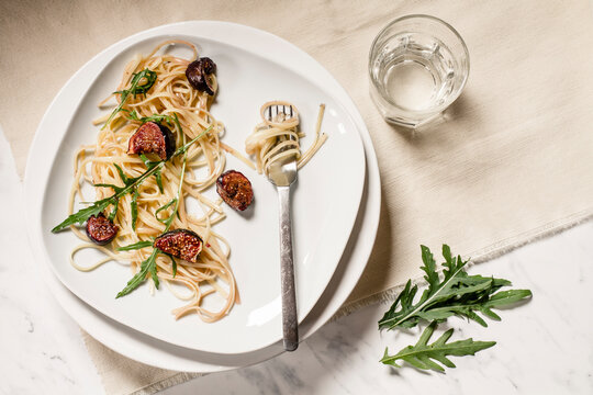 Plate with fig tagliatelle, rocket leaves, sauce and a glass of water, studio shot