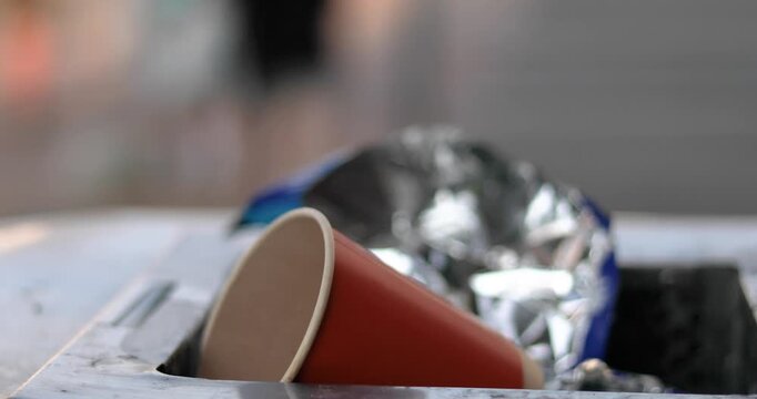 A disposable used cup thrown into a trash bin in a public place near a roadway.